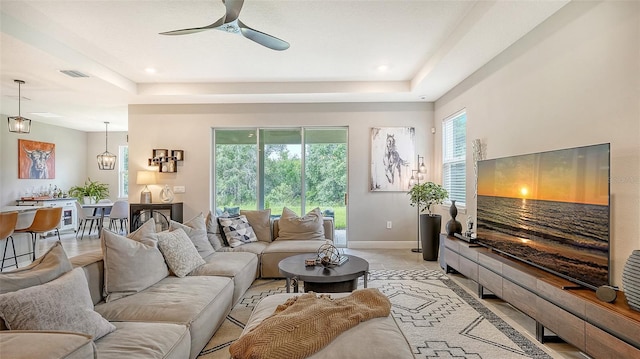 tiled living room featuring ceiling fan and a tray ceiling