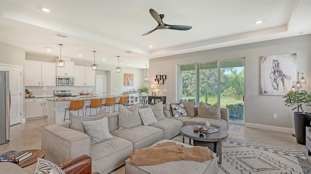 living room with light tile patterned floors, ceiling fan, and a raised ceiling