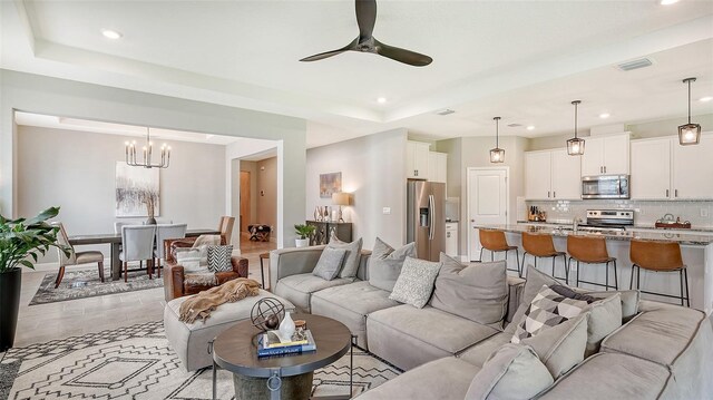 living room with a raised ceiling and ceiling fan with notable chandelier