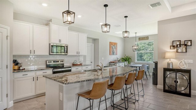 kitchen featuring appliances with stainless steel finishes, sink, a center island with sink, and hanging light fixtures