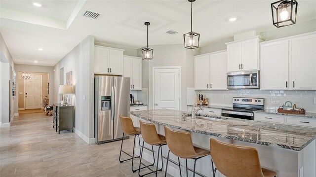 kitchen with tasteful backsplash, appliances with stainless steel finishes, white cabinets, sink, and decorative light fixtures