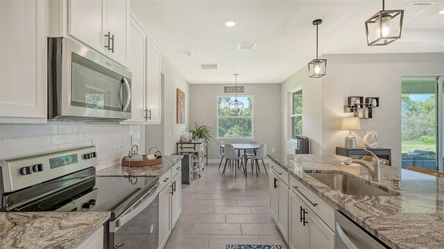 kitchen featuring decorative backsplash, white cabinetry, appliances with stainless steel finishes, light tile patterned flooring, and sink