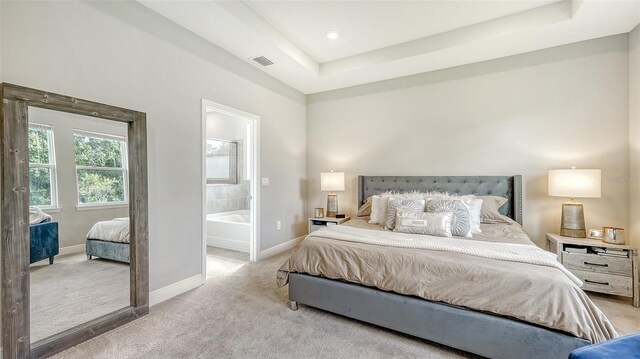 carpeted bedroom with ensuite bath and a tray ceiling