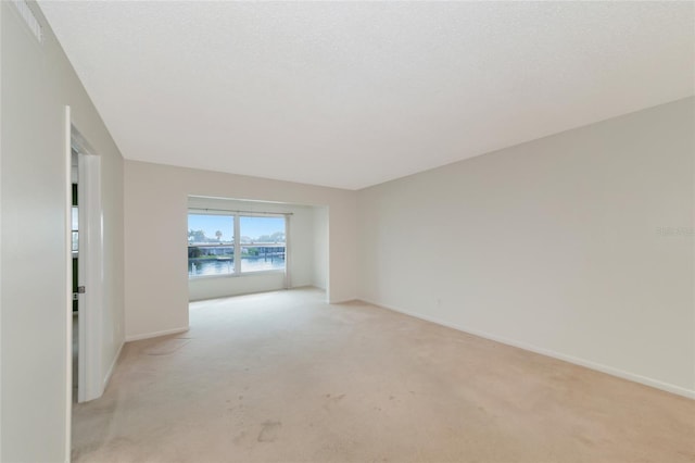 empty room featuring light colored carpet, a textured ceiling, and a water view