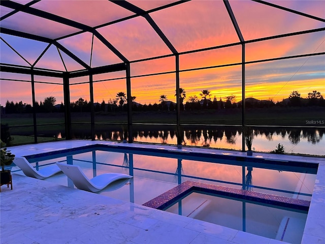 pool at dusk featuring glass enclosure, a water view, and a patio