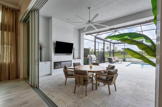 dining space featuring light hardwood / wood-style floors, a textured ceiling, ceiling fan, and a large fireplace