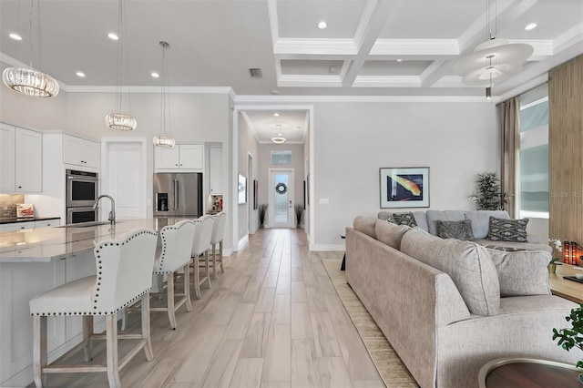 living room featuring coffered ceiling, a high ceiling, crown molding, a chandelier, and beam ceiling