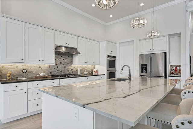 kitchen with pendant lighting, stainless steel appliances, a center island with sink, and a notable chandelier