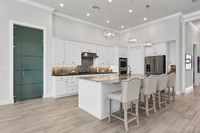 kitchen with decorative light fixtures, appliances with stainless steel finishes, light hardwood / wood-style floors, a kitchen bar, and a kitchen island with sink