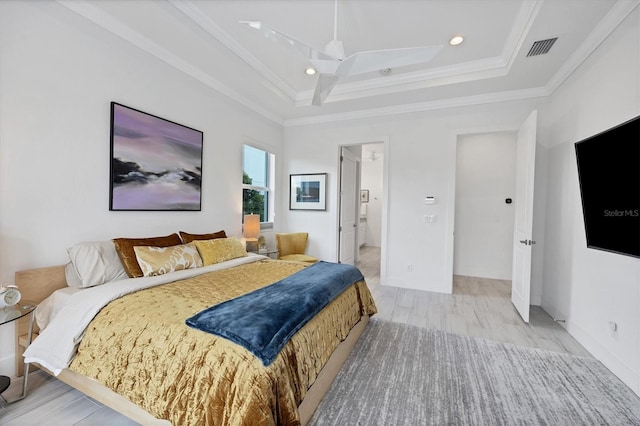 bedroom featuring crown molding, light wood-type flooring, a raised ceiling, and ensuite bathroom