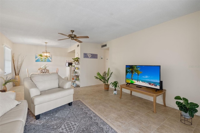 living room featuring ceiling fan with notable chandelier and a textured ceiling