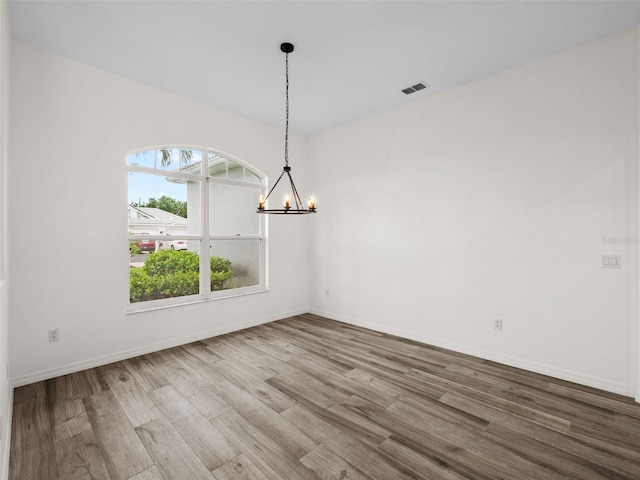 unfurnished dining area with wood-type flooring and a notable chandelier