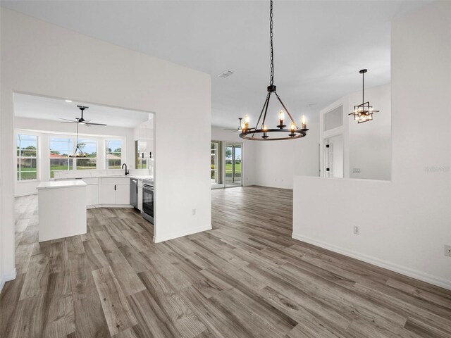 unfurnished living room featuring light hardwood / wood-style floors, ceiling fan with notable chandelier, and plenty of natural light