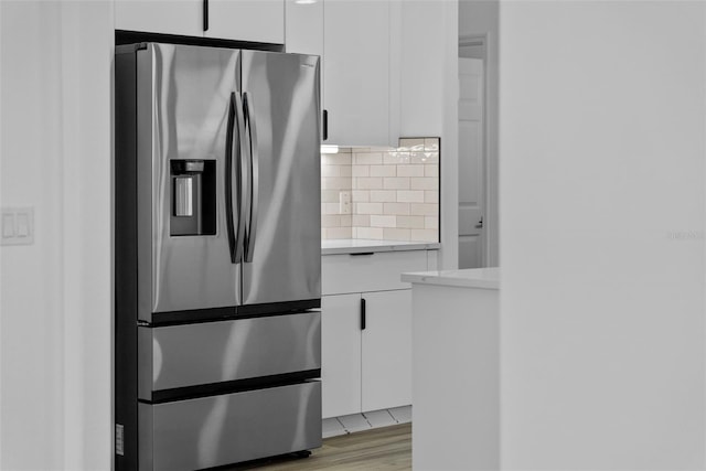 kitchen featuring stainless steel refrigerator with ice dispenser, white cabinetry, decorative backsplash, and light wood-type flooring