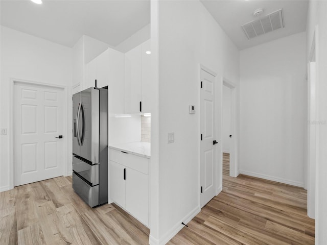 kitchen with white cabinetry, stainless steel fridge with ice dispenser, light wood-type flooring, and light stone countertops