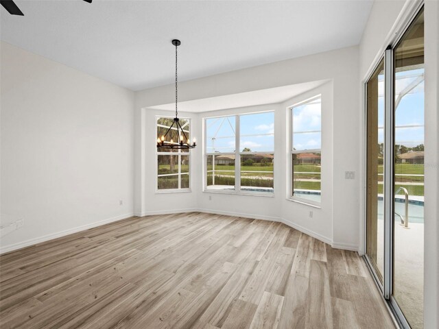 unfurnished dining area featuring ceiling fan with notable chandelier and light hardwood / wood-style flooring