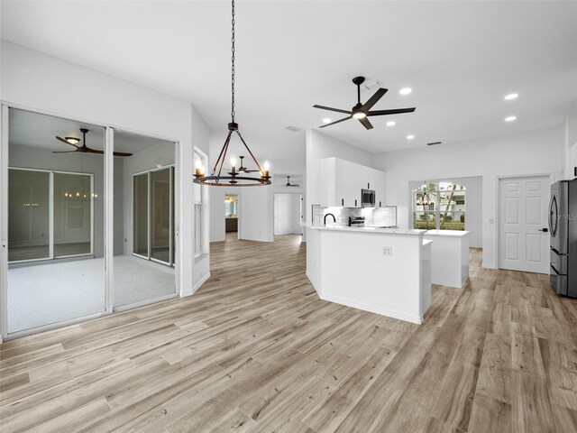 kitchen with light hardwood / wood-style flooring, white cabinets, ceiling fan with notable chandelier, stainless steel appliances, and decorative light fixtures