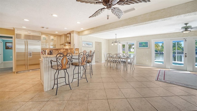 kitchen with light tile patterned flooring, decorative light fixtures, stainless steel built in fridge, ceiling fan, and wall chimney range hood