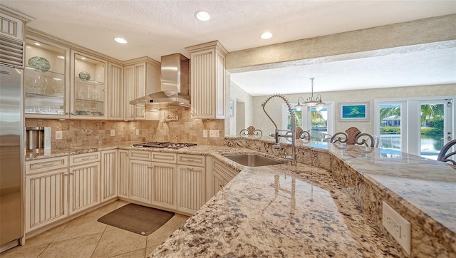 kitchen featuring wall chimney range hood, pendant lighting, and light stone countertops