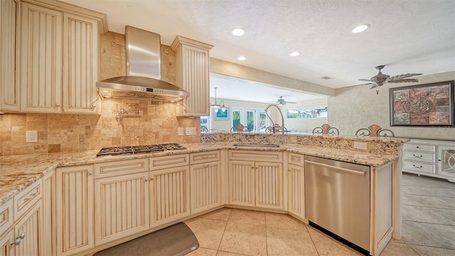 kitchen with a textured ceiling, stainless steel appliances, kitchen peninsula, ceiling fan, and wall chimney range hood