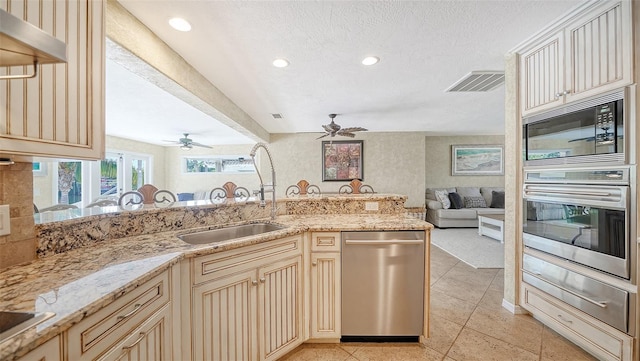 kitchen with appliances with stainless steel finishes, sink, light stone countertops, a textured ceiling, and cream cabinetry