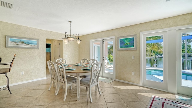 tiled dining area featuring french doors, a water view, and a chandelier