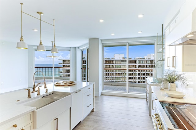 kitchen with light wood-type flooring, custom exhaust hood, white cabinets, and a healthy amount of sunlight