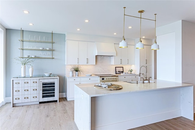 kitchen featuring stainless steel stove, white cabinetry, beverage cooler, hanging light fixtures, and custom range hood