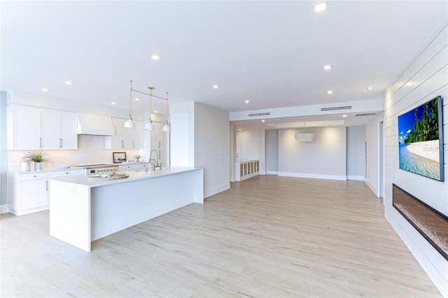 kitchen with premium range hood, tasteful backsplash, decorative light fixtures, a center island with sink, and white cabinets