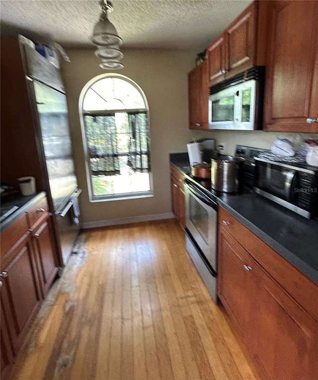 kitchen featuring a textured ceiling, light wood-type flooring, stainless steel appliances, and hanging light fixtures