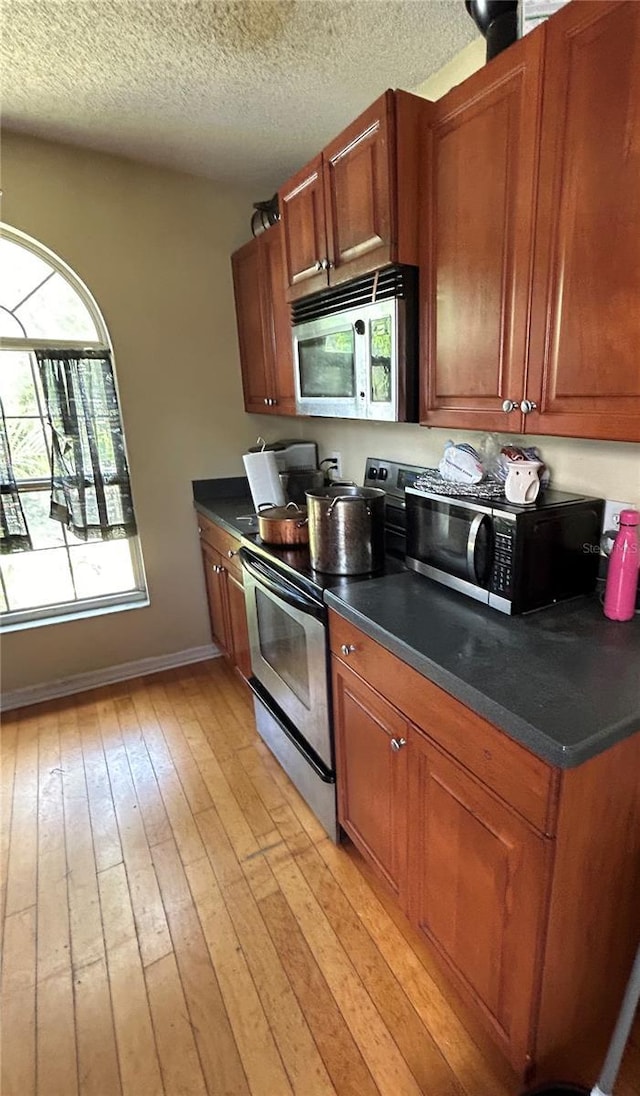 kitchen with appliances with stainless steel finishes, dark countertops, light wood-style flooring, and brown cabinets