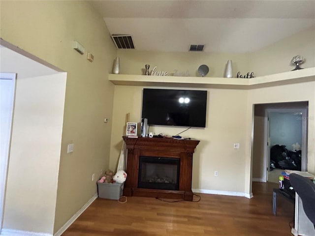 living area featuring a glass covered fireplace, visible vents, and wood finished floors