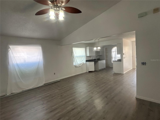 unfurnished living room featuring ceiling fan, vaulted ceiling, baseboards, dark wood-style floors, and a sink