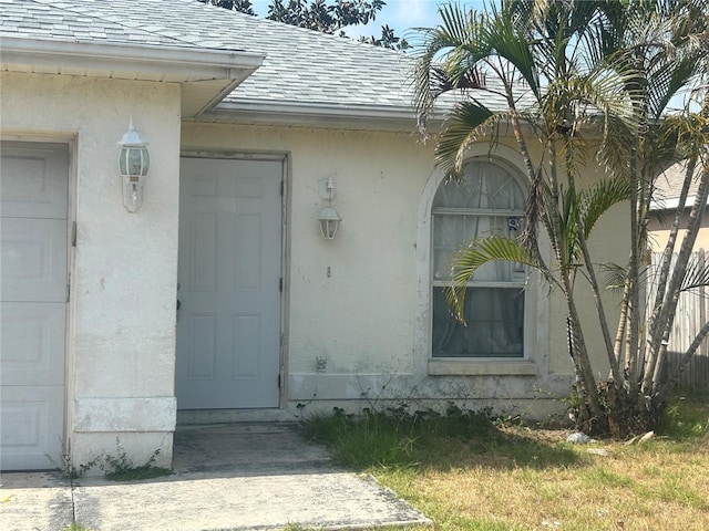 view of exterior entry featuring roof with shingles and stucco siding