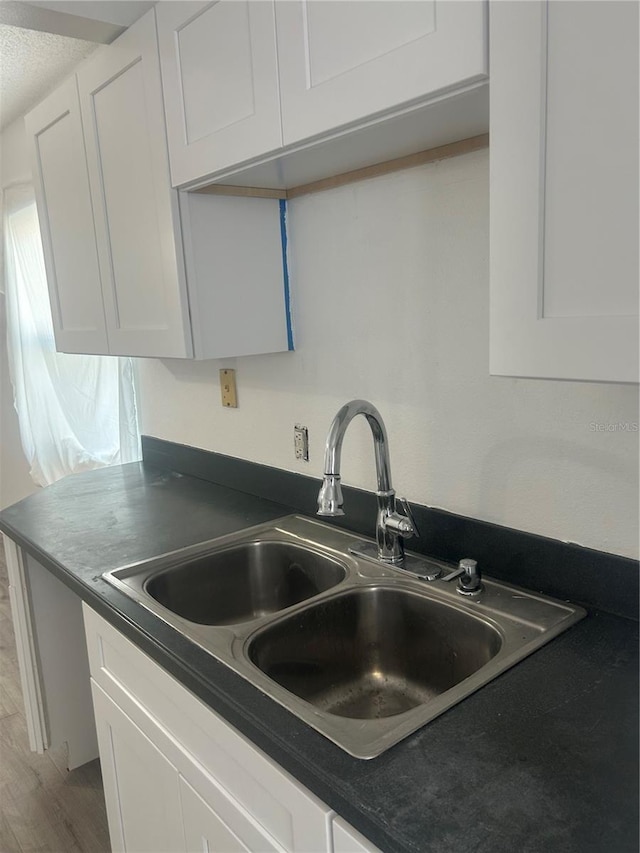 kitchen with a sink, dark countertops, white cabinets, and light wood-style floors