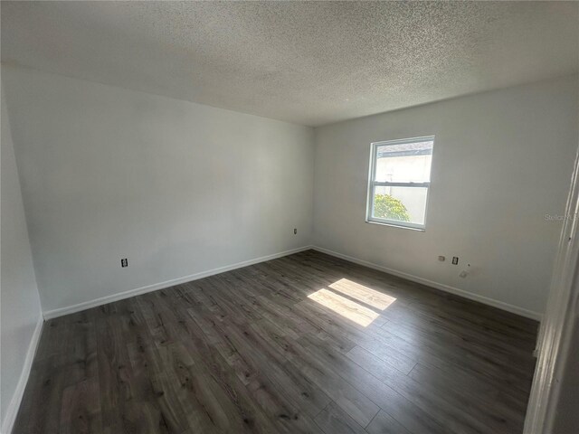 spare room featuring dark wood finished floors, a textured ceiling, and baseboards
