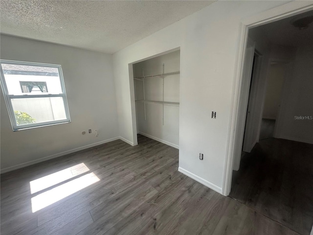 unfurnished bedroom featuring wood finished floors, a closet, a textured ceiling, and baseboards