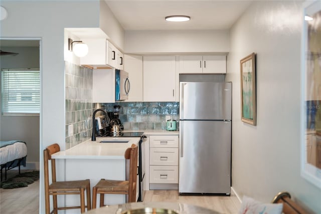 kitchen featuring light hardwood / wood-style floors, appliances with stainless steel finishes, white cabinets, backsplash, and a breakfast bar area