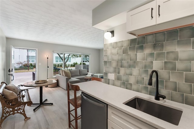 kitchen featuring light stone countertops, white cabinetry, sink, stainless steel dishwasher, and light hardwood / wood-style flooring