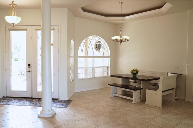 tiled dining area with a notable chandelier, a raised ceiling, and decorative columns