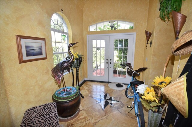 entryway with baseboards, french doors, a towering ceiling, a textured wall, and marble finish floor