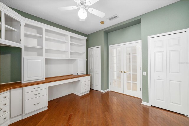 unfurnished office featuring ceiling fan, built in desk, and hardwood / wood-style floors