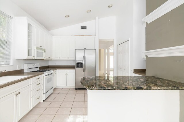 kitchen featuring white appliances, light tile patterned floors, dark stone counters, white cabinets, and vaulted ceiling