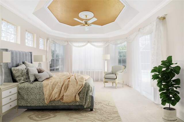 bedroom featuring ceiling fan, crown molding, a tray ceiling, and light colored carpet