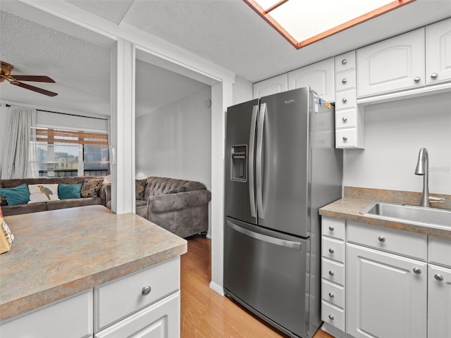 kitchen with stainless steel refrigerator with ice dispenser, sink, white cabinetry, light wood-type flooring, and ceiling fan