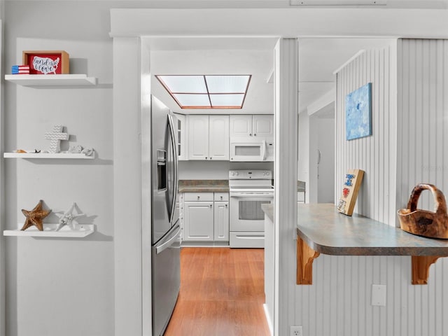 kitchen featuring a skylight, a breakfast bar area, white cabinets, light hardwood / wood-style floors, and white appliances