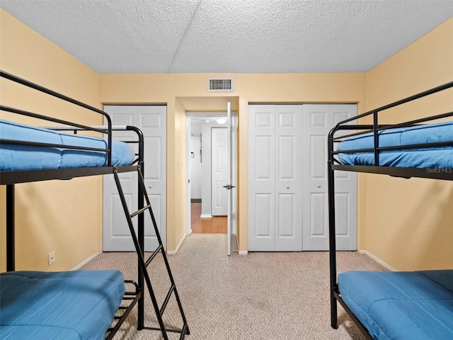 carpeted bedroom featuring two closets and a textured ceiling