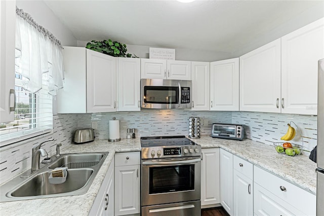 kitchen with appliances with stainless steel finishes, white cabinetry, backsplash, light stone counters, and sink