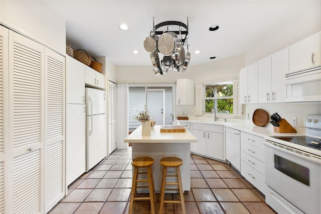 kitchen with sink, a breakfast bar area, a kitchen island, white cabinetry, and white appliances