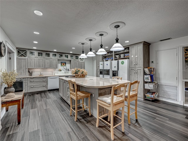 kitchen featuring tasteful backsplash, white appliances, gray cabinetry, a kitchen island, and hardwood / wood-style flooring